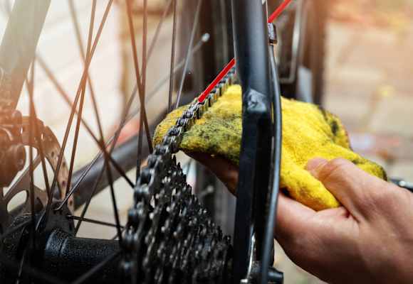 Hand die mit rotem Schlauch und gelbem Lappen eine Fahrradkette schmiert 