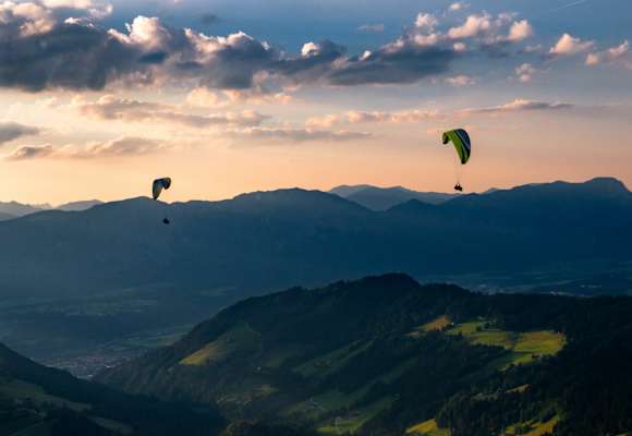 Zwei Personen paragleiten über ein Tal in der Wildschönau.